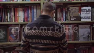 一个年轻人在书店里<strong>选择</strong>一本书，然后转过身来<strong>面对</strong>相机。